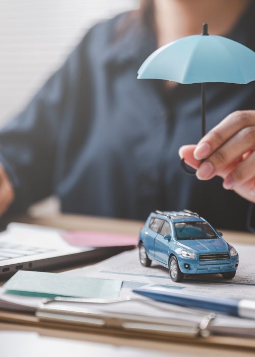 Car insurance protect safe transport. Safety trust. Protection secure assurance. A woman is holding a blue umbrella over a toy car on a desk.