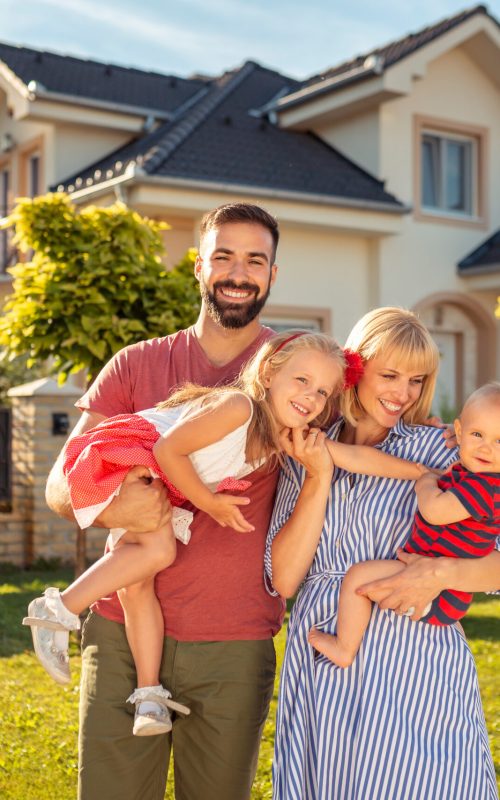 Parents and children having fun standing in front of their new house